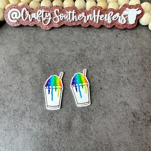 May include: Two rainbow-colored snow cone cups with a white background and a brown straw. The snow cone is dripping down the side of the cup.