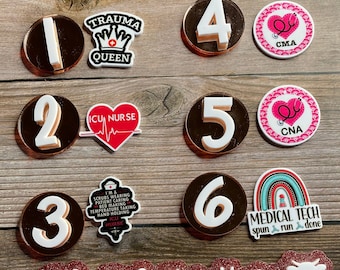 May include: A set of 6 round, brown and white resin ornaments with numbers 1 through 6. Each ornament has a different design, including a crown, a heart with a stethoscope, a rainbow, and a medical symbol. The ornaments are perfect for a medical themed party or as gifts for medical professionals.