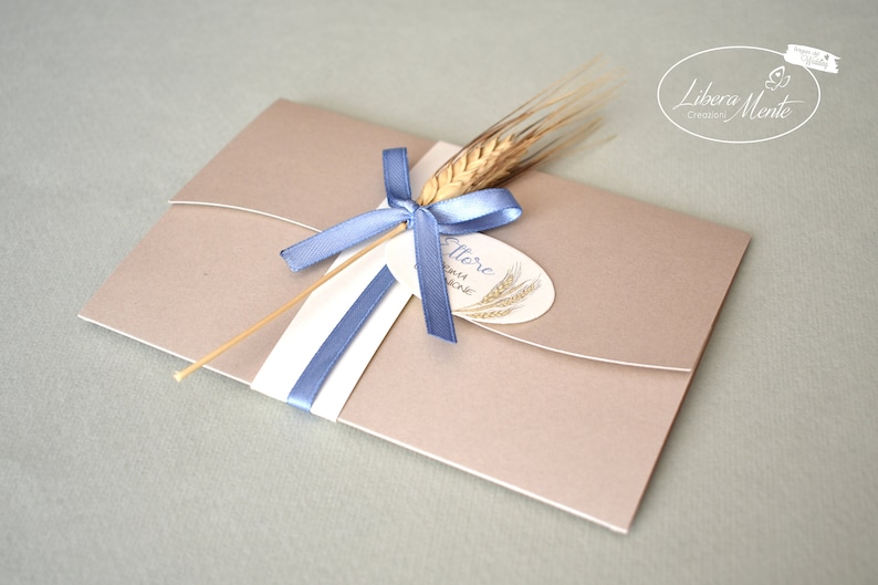 May include: A light brown envelope with a blue ribbon and a wheat stalk tied to it. The envelope has a white label with the text "Offre" and a wheat stalk design.