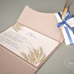 May include: A beige invitation card with a wheat design and the text "Lettore" in blue. The card is folded in half and has a blue ribbon tied around it. The ribbon is attached to a small tag with the text "Lettore" in blue.