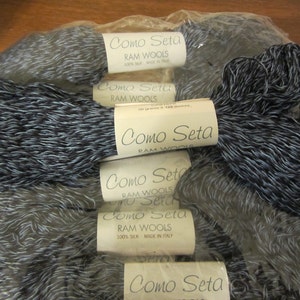 May include: A close-up of several skeins of Como Seta yarn, a 100% silk yarn made in Italy. The yarn is a blend of black and silver, creating a subtle, elegant look. The labels on the skeins read "Como Seta" and "RAM WOOLS".
