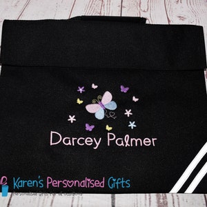 Puede incluir: Mochila negra para libros con rayas blancas en el lateral. La mochila tiene un dise&ntilde;o de mariposa con detalles en rosa, morado y amarillo. El nombre "Darcey Palmer" est&aacute; bordado en la mochila.