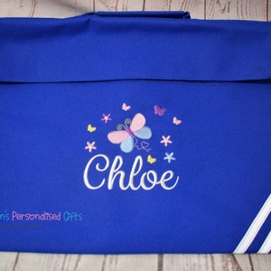 Puede incluir: Una mochila azul real con ribetes blancos. La mochila tiene un dise&ntilde;o bordado de mariposa y flores con el nombre "Chloe" bordado en blanco.