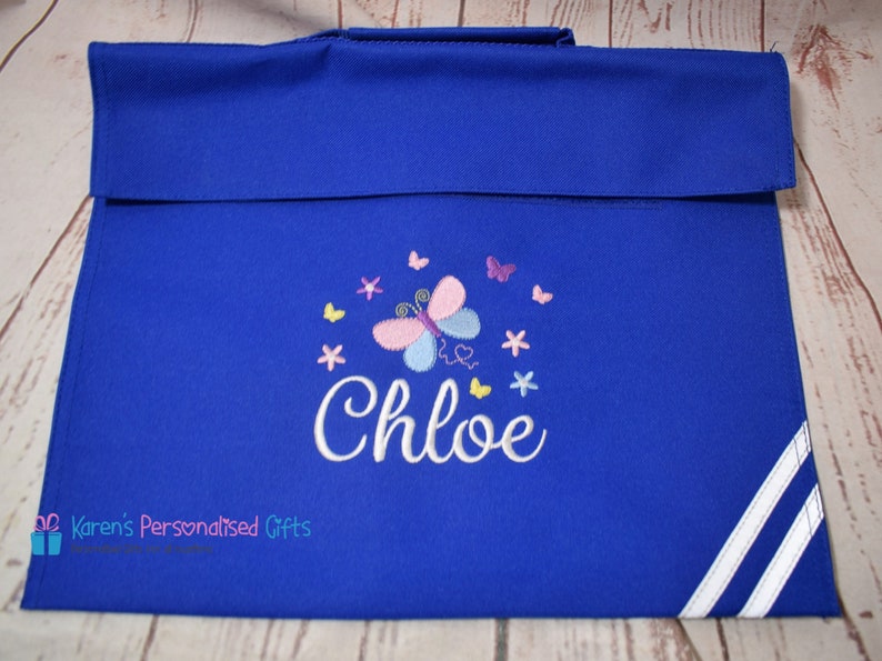 Puede incluir: Una mochila azul real con ribetes blancos. La mochila tiene un dise&ntilde;o bordado de mariposa y flores con el nombre "Chloe" bordado en blanco.