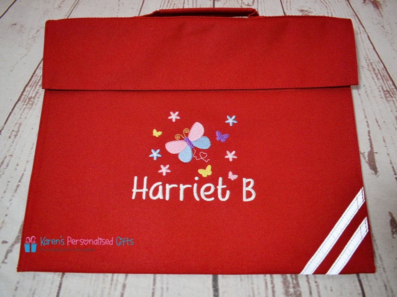 Puede incluir: Mochila roja con correas blancas y un dise&ntilde;o de mariposa bordado en la parte delantera. La mochila est&aacute; personalizada con el nombre "Harriet B."