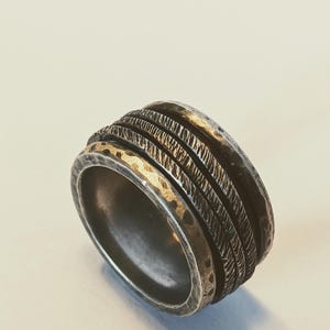 Könnte beinhalten: Ein silberner Ring mit einer strukturierten, gehämmerten Oberfläche. Der Ring hat mehrere Bänder mit unterschiedlichen Mustern.