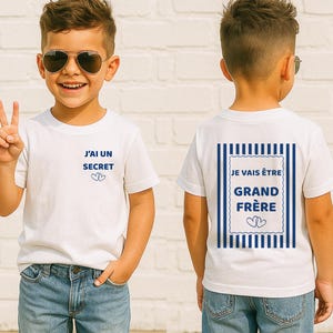 Peut inclure: Un t-shirt blanc à manches courtes avec du texte bleu. L'avant affiche 'J'AI UN SECRET' avec deux cœurs. Le dos présente un motif rectangulaire à rayures bleues avec le texte 'JE VAIS ÊTRE GRAND FRÈRE' et deux cœurs sous les mots.