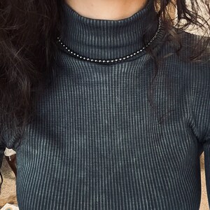 May include: A close-up of a person wearing a dark blue turtleneck sweater with a silver beaded necklace.