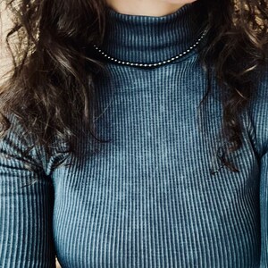 May include: A close-up of a person wearing a dark blue ribbed turtleneck shirt. The shirt has a subtle sheen and a slightly textured surface.