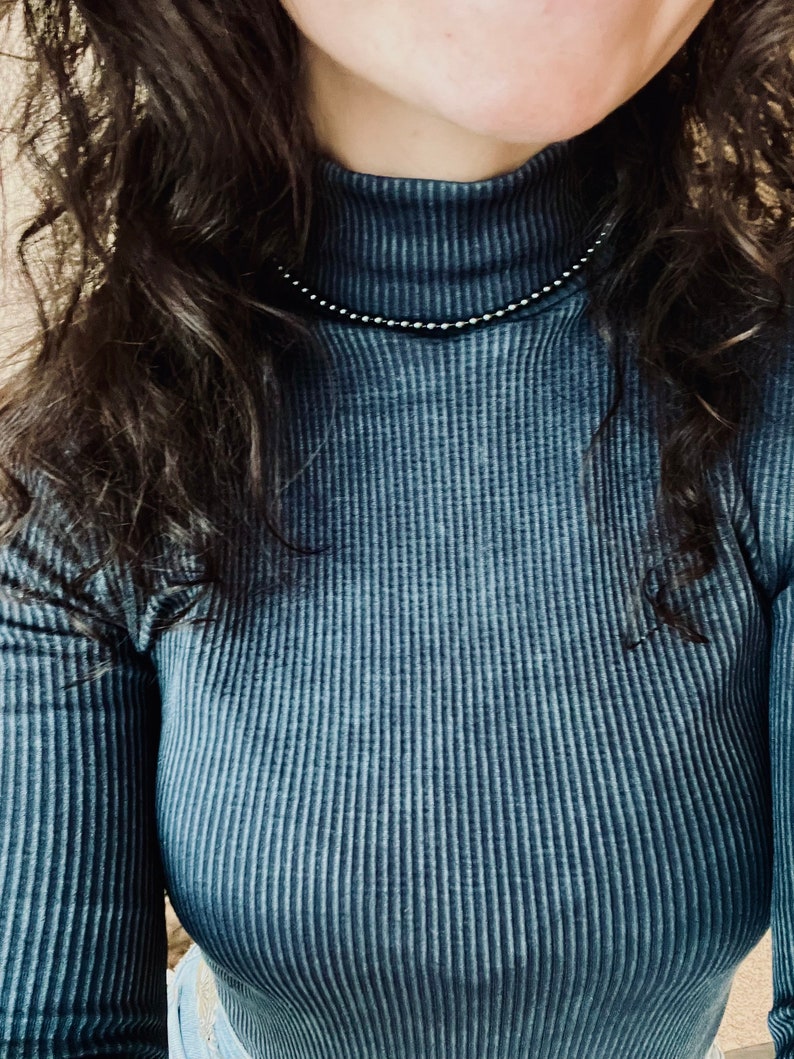 May include: A close-up of a person wearing a dark blue ribbed turtleneck shirt. The shirt has a subtle sheen and a slightly textured surface.
