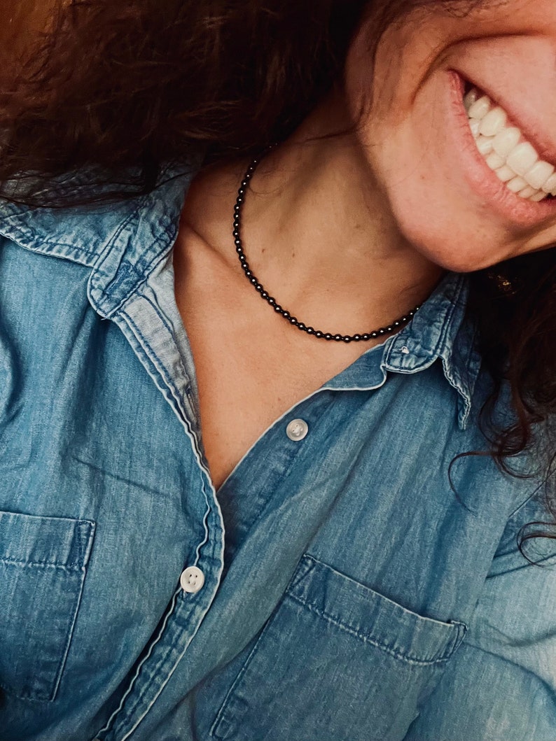 May include: A woman wearing a denim shirt with a black beaded necklace.