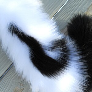 May include: A black and white faux fur tail with a long, fluffy white section and a shorter, black section.