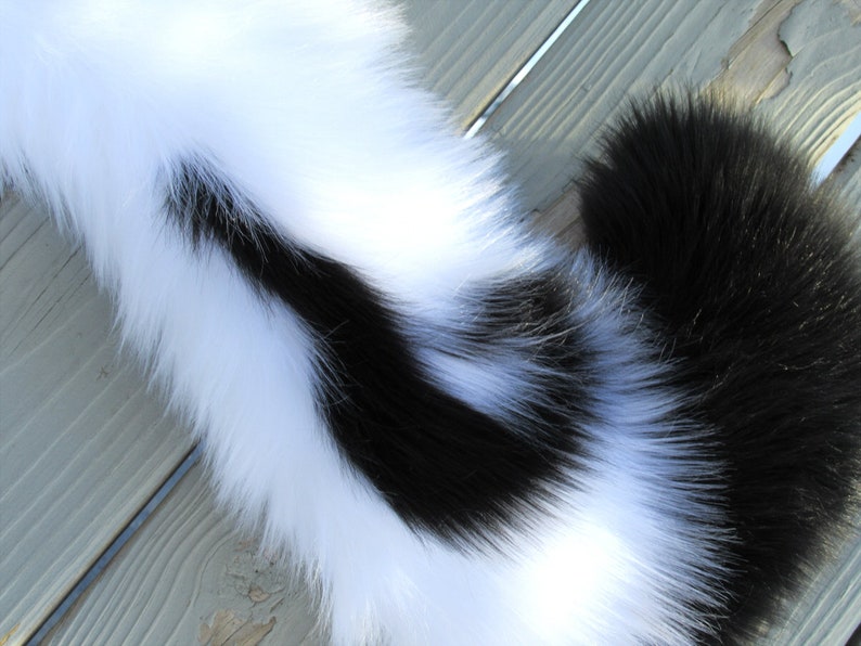 May include: A black and white faux fur tail with a long, fluffy white section and a shorter, black section.