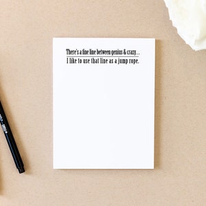 May include: A white notepad with a black line drawn across it. The notepad has the text "There's a fine line between genius & crazy... I like to use that line as a jump rope." printed on it.