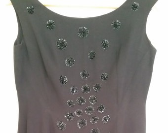 May include: A black sleeveless dress with a scoop neck and a pattern of black flower-shaped sequins.