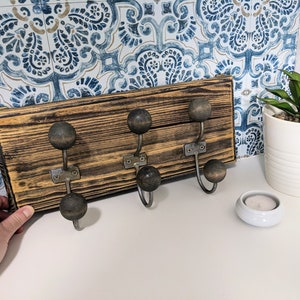 May include: A wooden coat rack with five hooks. The hooks are made of metal and have round black knobs. The wood is dark brown and has a distressed finish.