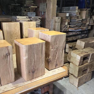 May include: A collection of unfinished, rectangular wooden blocks and beams. The blocks are various sizes, with a natural wood grain and a light brown color. Some blocks are stacked, while others stand upright on a wooden table.