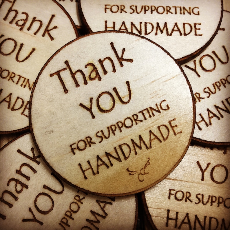 May include: Close-up of several round wooden tags with the text "Thank You" and "For Supporting Handmade" engraved on them. The tags are stacked on top of each other.
