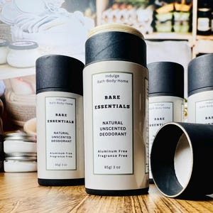 May include: Several cylindrical deodorant containers with black lids and labels that read "Bare Essentials Natural Unscented Deodorant." The containers are white with black text and a beige border. The product is aluminum and fragrance free.
