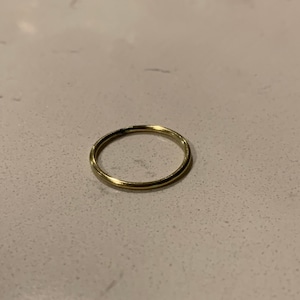 Puede incluir: Un anillo delgado de color dorado. El anillo es circular y parece estar hecho de metal. El anillo est&aacute; sobre una superficie clara y moteada.