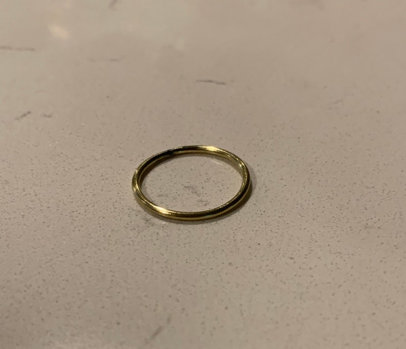 Puede incluir: Un anillo delgado de color dorado. El anillo es circular y parece estar hecho de metal. El anillo est&aacute; sobre una superficie clara y moteada.