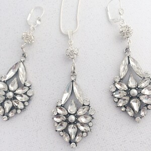 May include: A silver necklace and earrings set with crystal teardrop pendants. The pendants are adorned with clear rhinestones and a single pearl in the center.