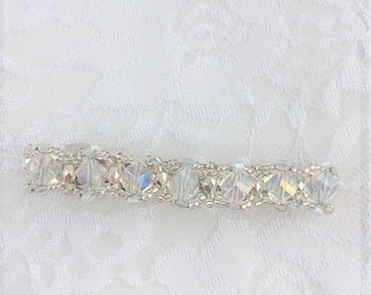 May include: A silver hair clip with clear crystal beads. The clip is on a white lace background.