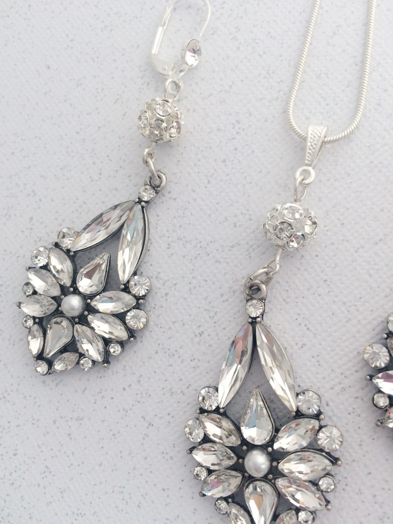 May include: A silver necklace and earrings set with crystal teardrop and round accents. The necklace has a delicate chain and the earrings have a clip-on closure.