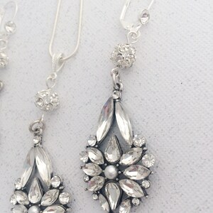 May include: A silver necklace and earrings set with a crystal flower pendant and a small crystal ball charm.