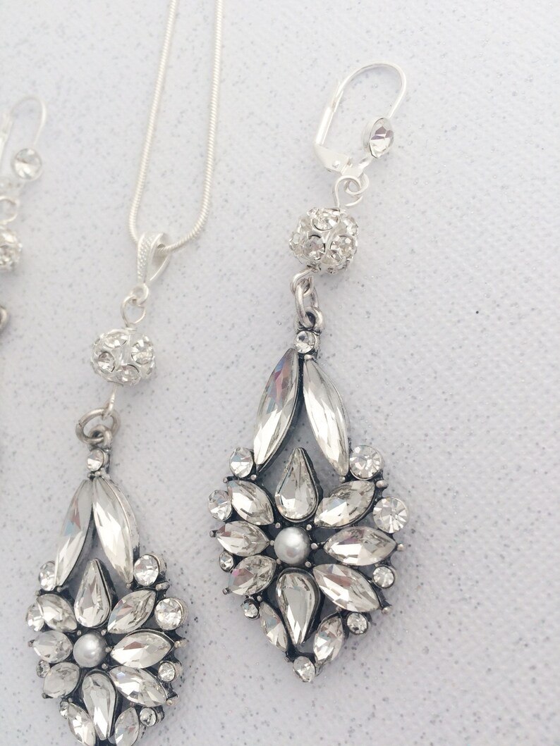 May include: A silver necklace and earrings set with a crystal flower pendant and a small crystal ball charm.