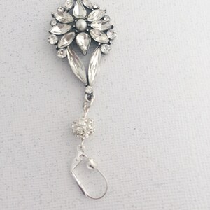 May include: Silver dangle earrings with a crystal flower design and a small crystal ball charm.