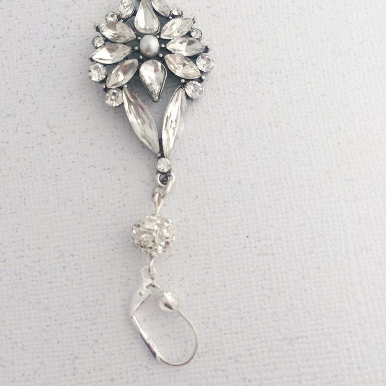 May include: Silver dangle earrings with a crystal flower design and a small crystal ball charm.