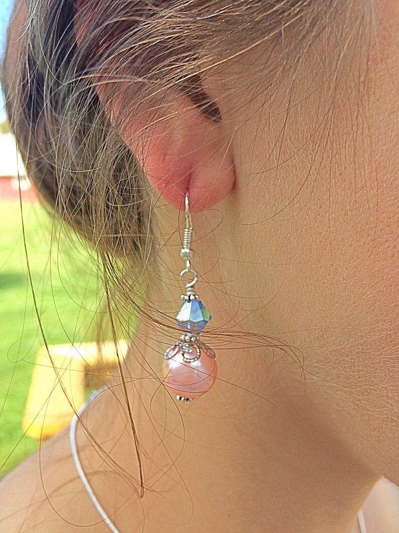 Puede incluir: Un par de pendientes colgantes con una perla rosa y un cristal azul. Los pendientes son de plata y tienen un dise&ntilde;o delicado.