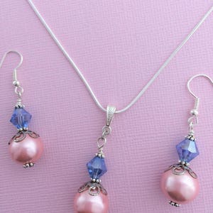 Puede incluir: Un collar de cadena de plata y pendientes a juego con un colgante de perla rosa y cristal azul.
