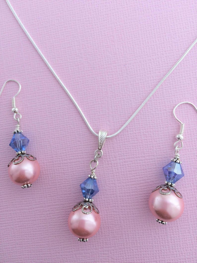 Puede incluir: Un collar de cadena de plata y pendientes a juego con un colgante de perla rosa y cristal azul.