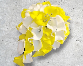 Puede incluir: Un ramo de novia con calas amarillas y blancas. El arreglo está adornado con pequeñas perlas y adornos brillantes. Las flores están dispuestas en cascada sobre un fondo gris.