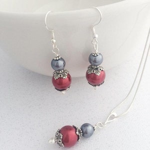 May include: A silver necklace and earrings set with red and gray pearl beads. The necklace has a silver chain and the earrings have silver hooks.