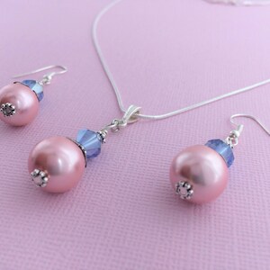 Puede incluir: Un delicado collar de plata y pendientes a juego con una perla rosa y un acento de cristal azul. El conjunto es perfecto para a&ntilde;adir un toque de elegancia a cualquier atuendo.