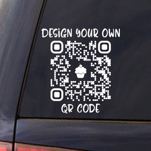 May include: White decal on a car window featuring a QR code with a cupcake icon in the center. The text "DESIGN YOUR OWN" is above the code, and "QR CODE" is below. The decal is designed to be applied to a car window.