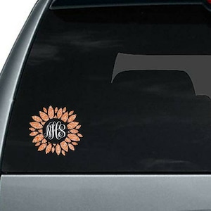 May include: A copper glitter sunflower decal with the monogram "MHS" in the center. The decal is on a black car window.