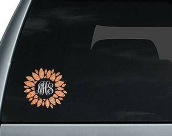 May include: A copper glitter sunflower decal with the monogram "MHS" in the center. The decal is on a black car window.