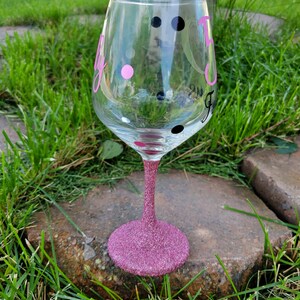 May include: A pink glitter wine glass with black and pink polka dots and the word "Fly" written on it.