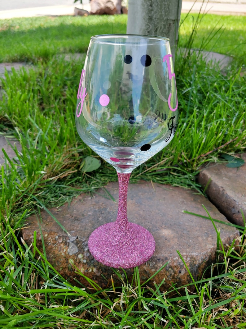 May include: A pink glitter wine glass with black and pink polka dots and the word "Fly" written on it.