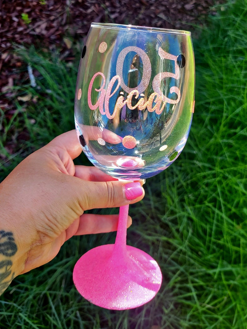 May include: A pink stemless wine glass with black polka dots and gold glitter. The glass has the number "30" and the name "Alicia" written on it.