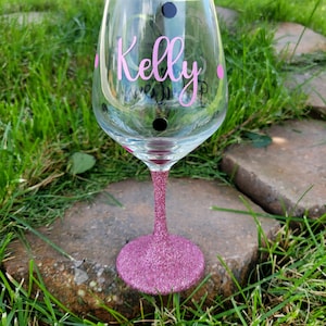May include: A pink glitter wine glass with black polka dots and the name "Kelly" written in pink on the side.