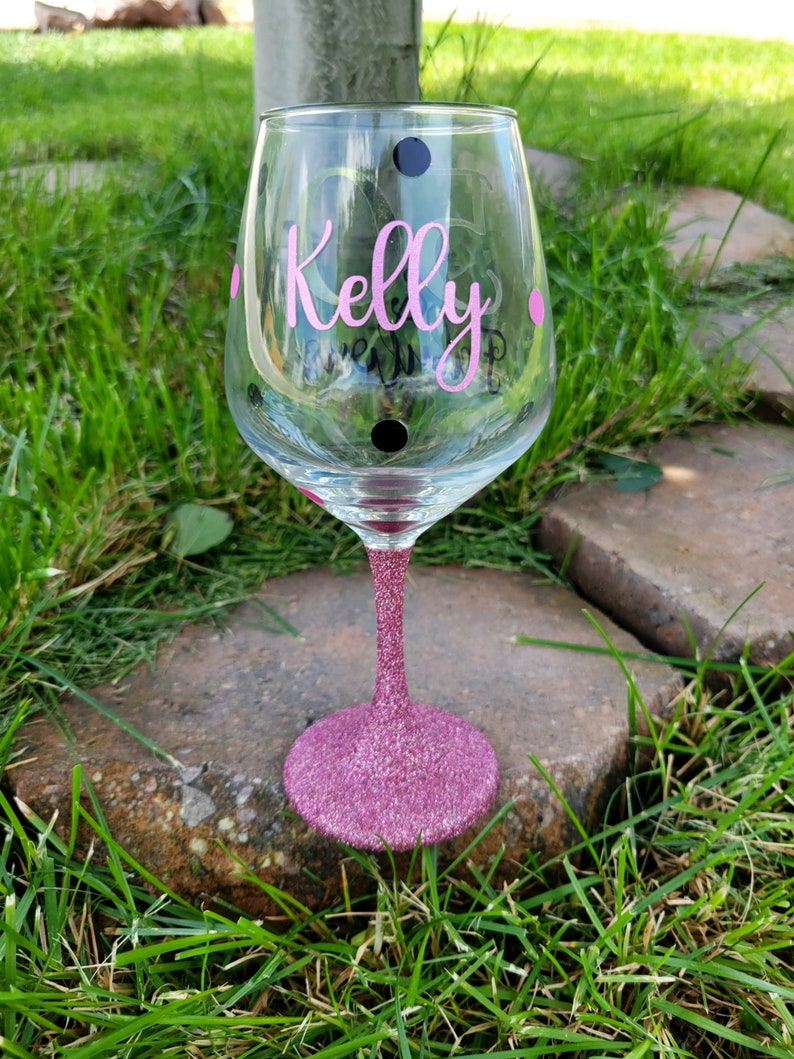 May include: A pink glitter wine glass with black polka dots and the name "Kelly" written in pink on the side.