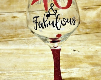 May include: A clear wine glass with a pink glitter stem and base. The glass has black polka dots and the text "40 & Fabulous" in black and red lettering.