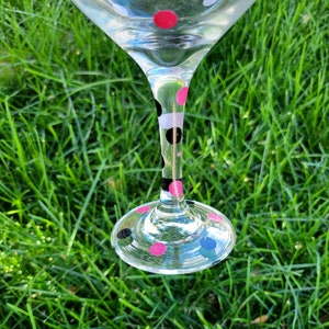 May include: A clear glass wine glass with a black and white polka dot pattern and pink polka dots on the stem and base.