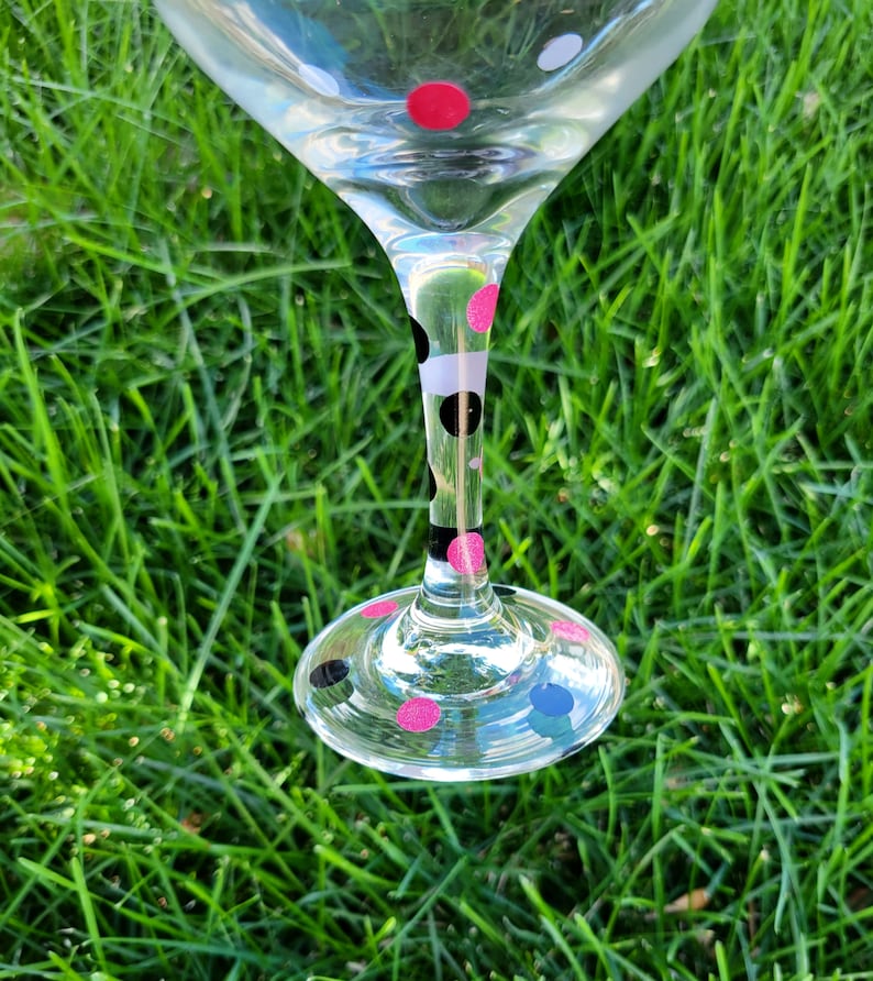 May include: A clear glass wine glass with a black and white polka dot pattern and pink polka dots on the stem and base.