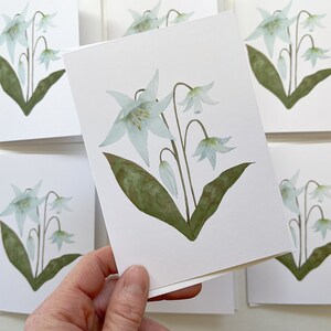 Easter Lily botanical watercolor painting printed onto a white card. Image is centred on a white cardstock background. Close detail of the card in foreground, multiples of same card in background.